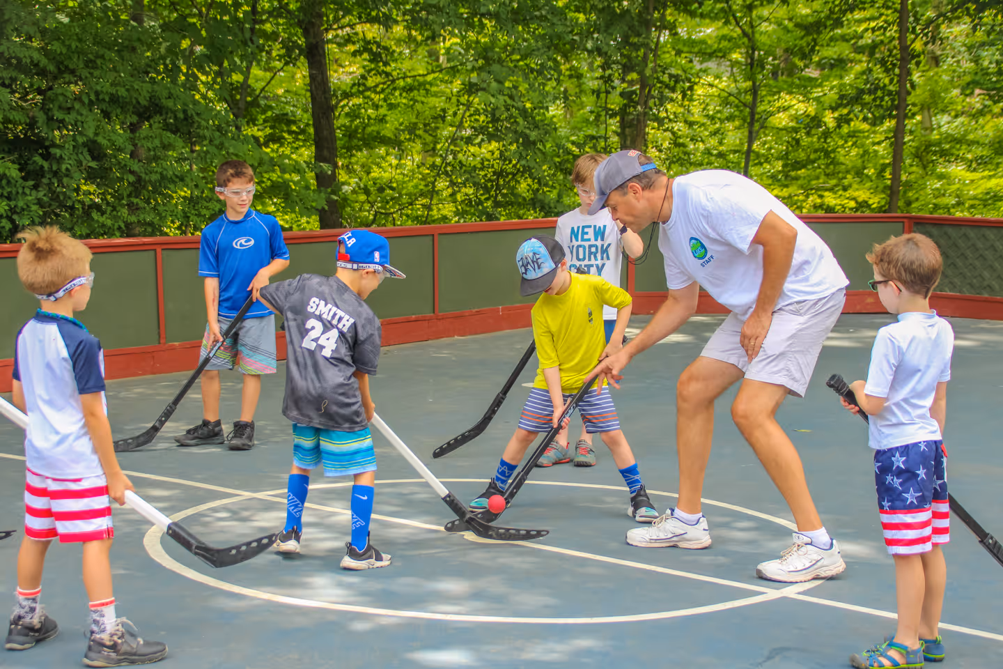 Group of young boys playing street hockey outdoors with coach dropping a ball for face-off.