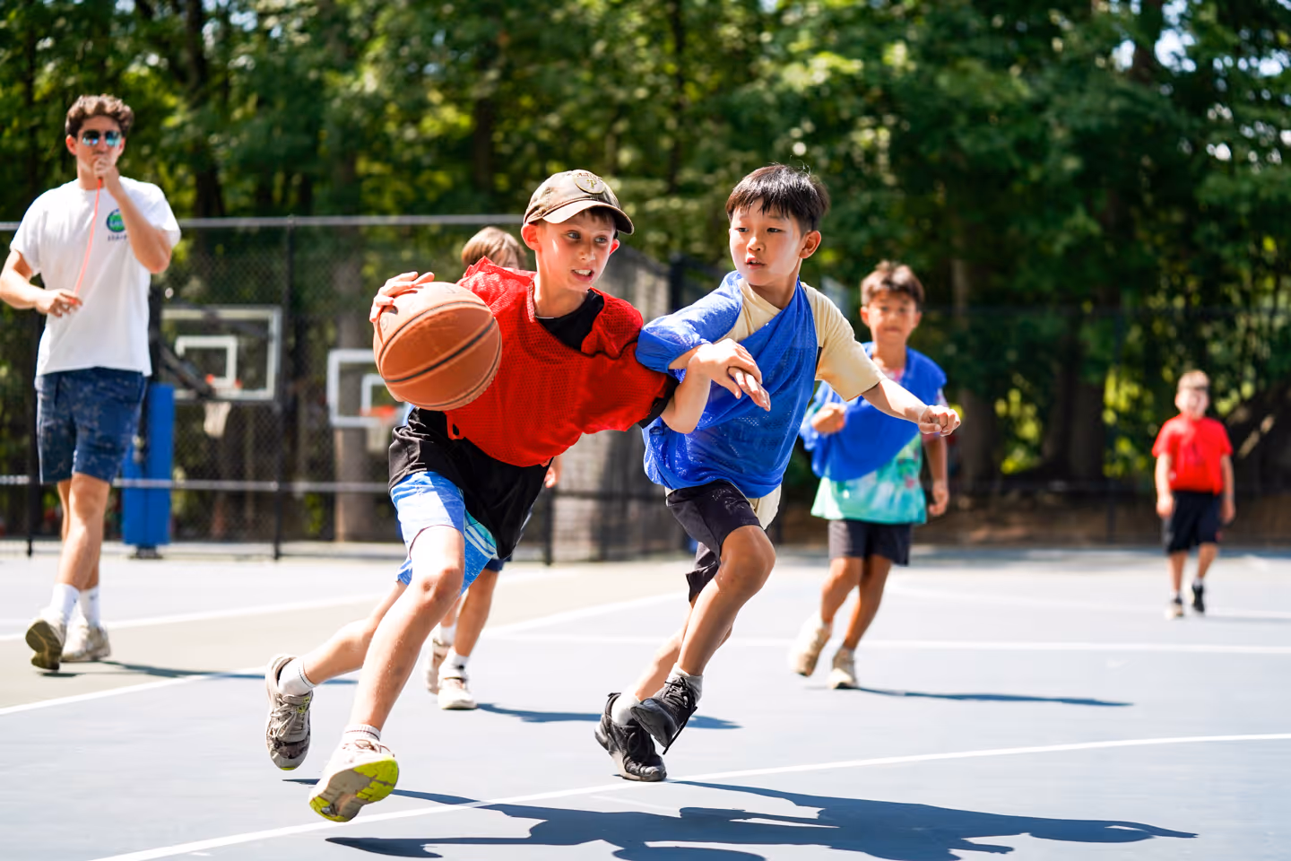 Two boys playing basketball outdoors, one dribbling the ball while the other defends closely.