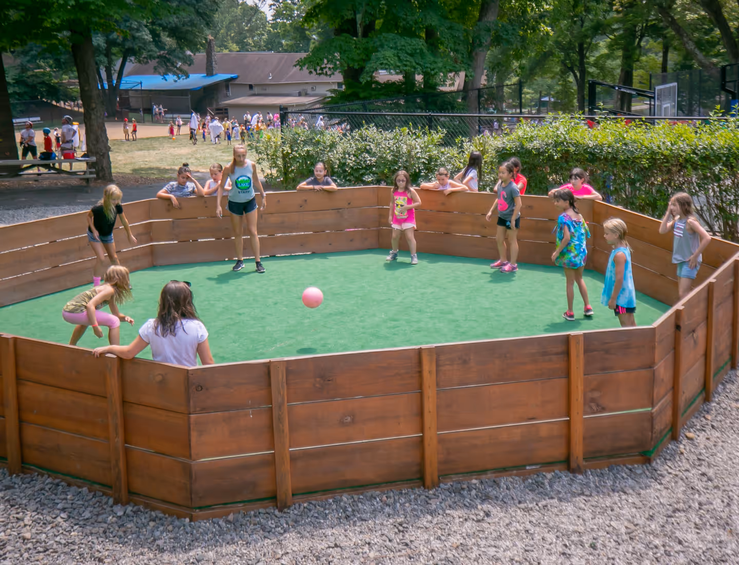 Group of children and a female staff member playing gaga inside a wooden court at camp.