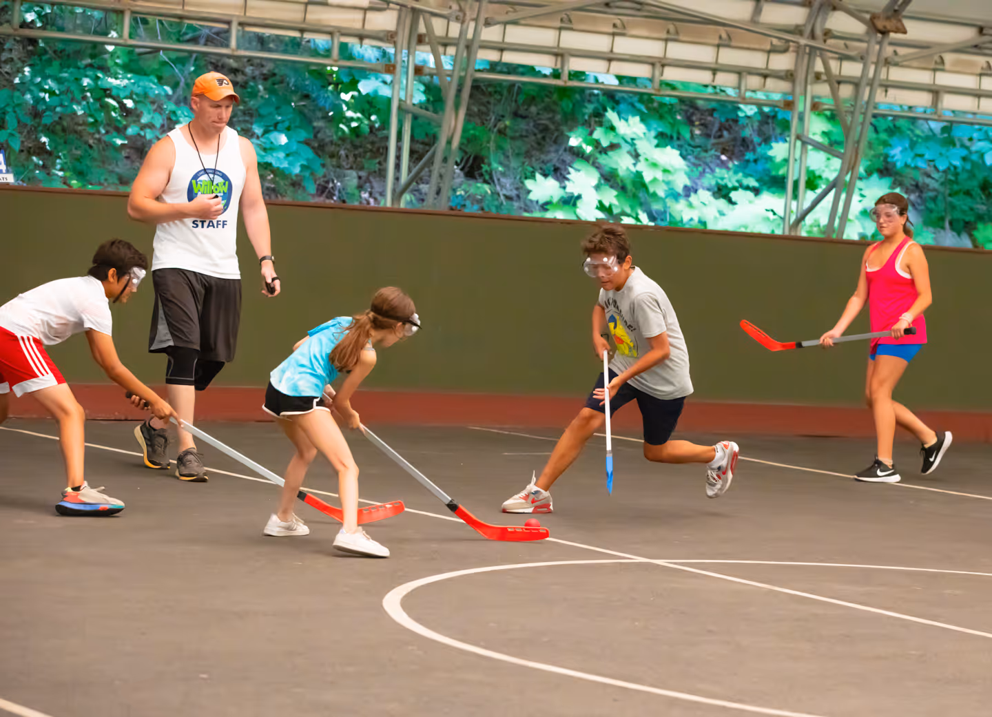 Four campers wearing goggles playing floor hockey with a coach observing.