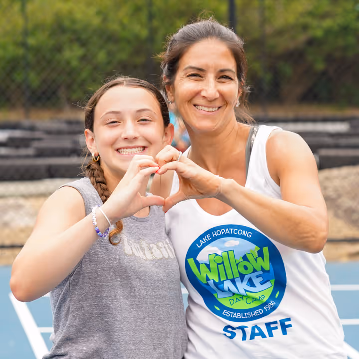 Two smiling females, one wearing a Willow Lake staff tank top, making a heart shape with their hands.