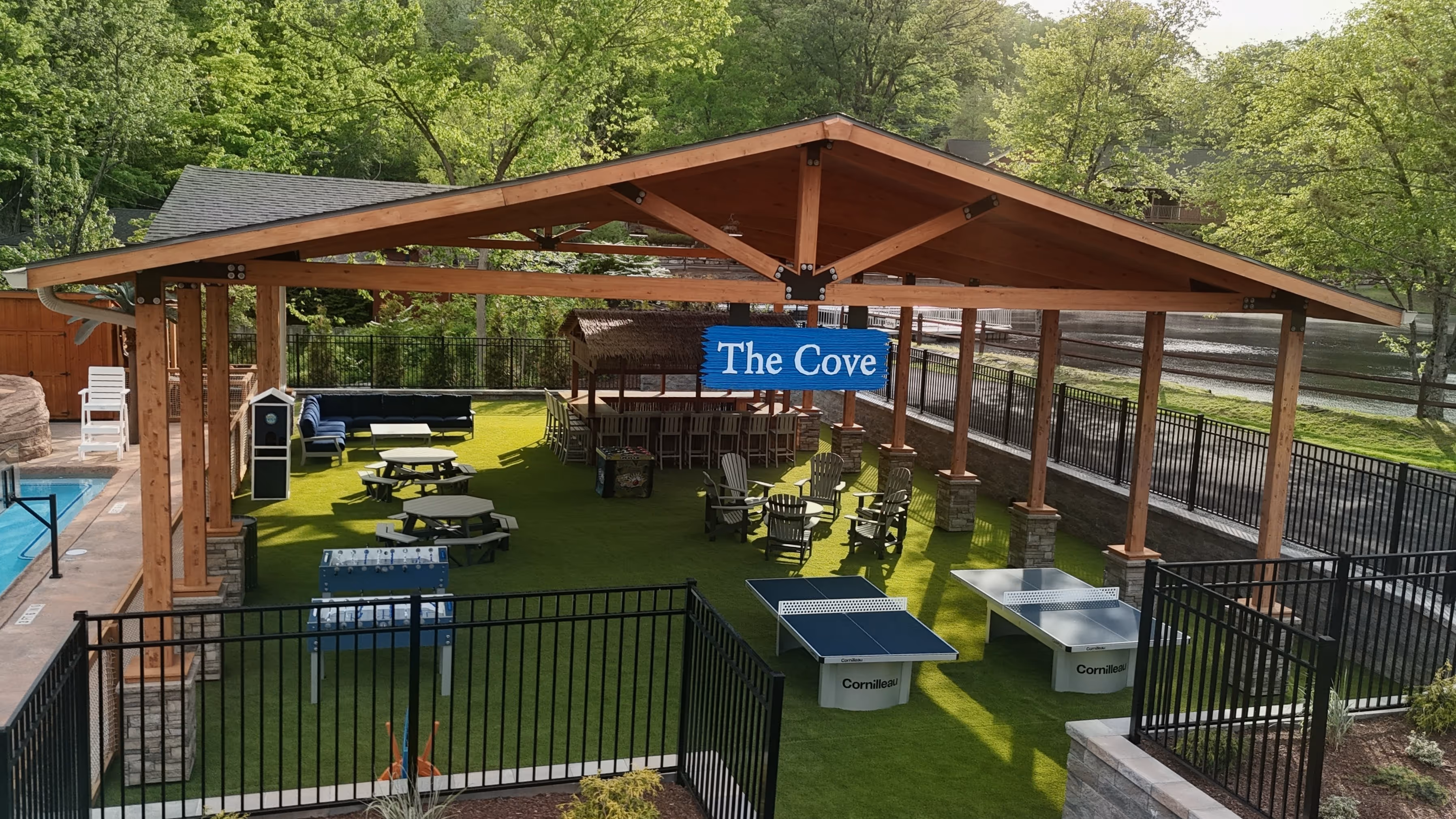 Outdoor covered recreational area called The Cove with games, seating, tables, and a bar near a pool.