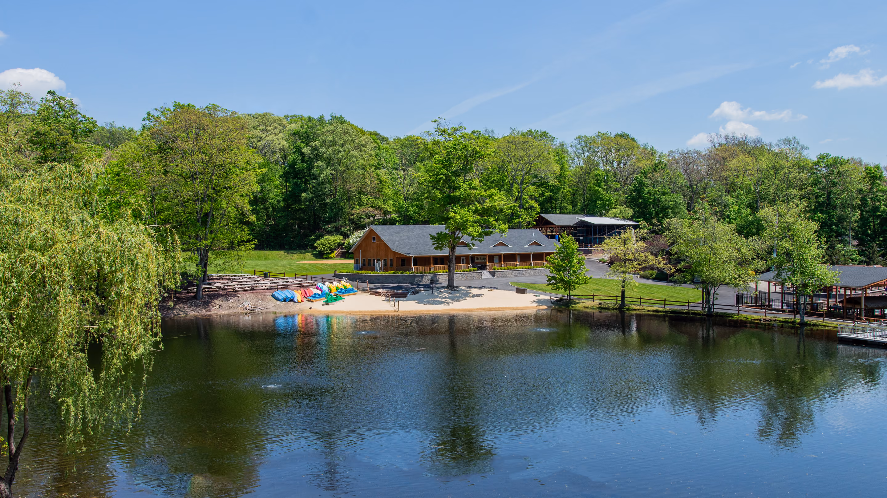 Red lodge building beside a calm lake surrounded by green trees and reflected in the water.