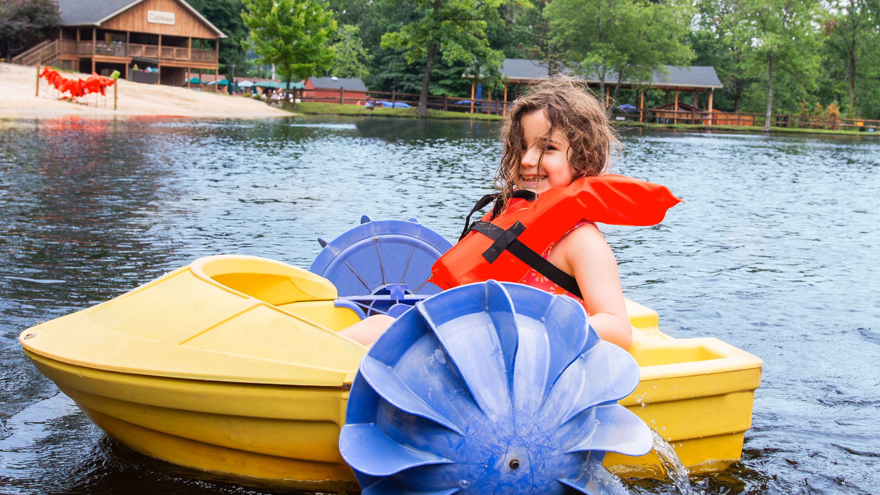 Two people in orange life jackets paddling a blue canoe on a calm lake.