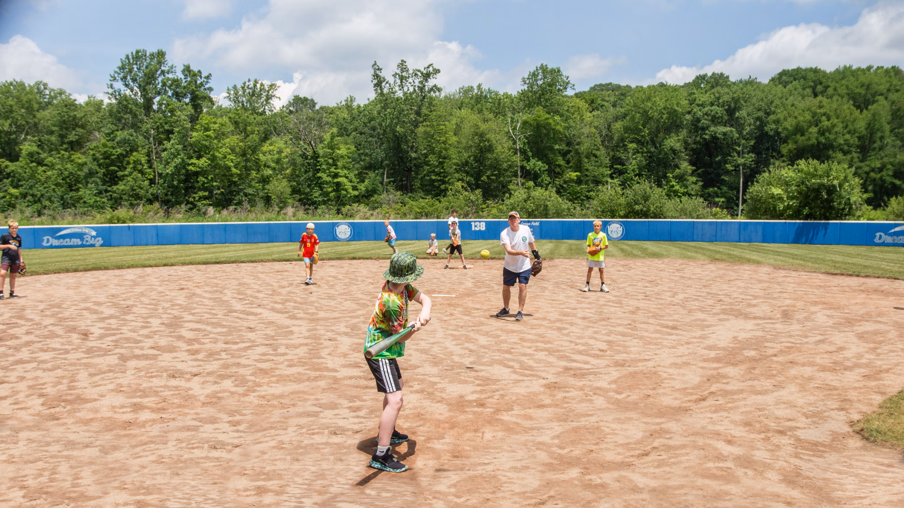 Young boy in navy shirt and shorts crouching on green grass holding a red kickball.
