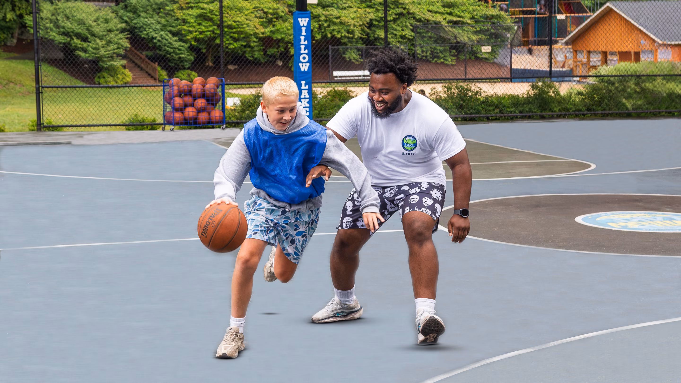 Camp staff member teaching young boys to play pickleball on an outdoor court.