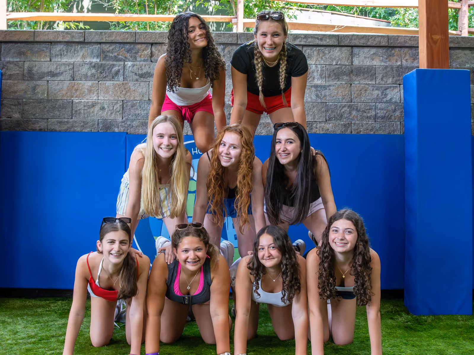 Group of smiling girls dressed in blue building a sandcastle together outdoors.
