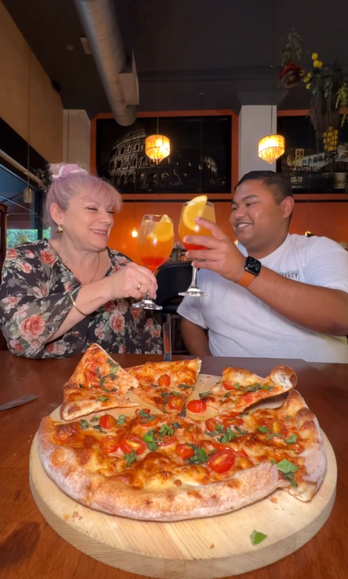 Obi and restaurant owner of Amante Restaurant in Downton Los Angeles cheers their cocktails with a pizza on the table.