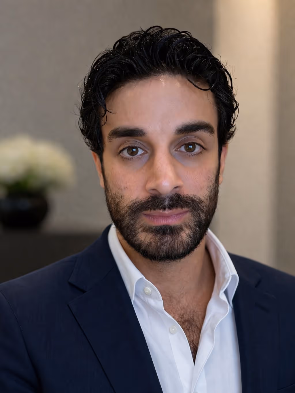 Portrait of a man with dark hair and beard wearing a navy blazer and white shirt.