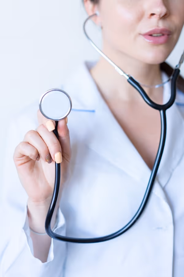 Close-up of a healthcare professional in a white coat holding a stethoscope toward the camera.