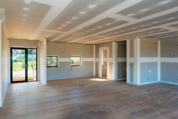 Empty room under construction with drywall, two small windows, sliding glass door, and wooden floor.