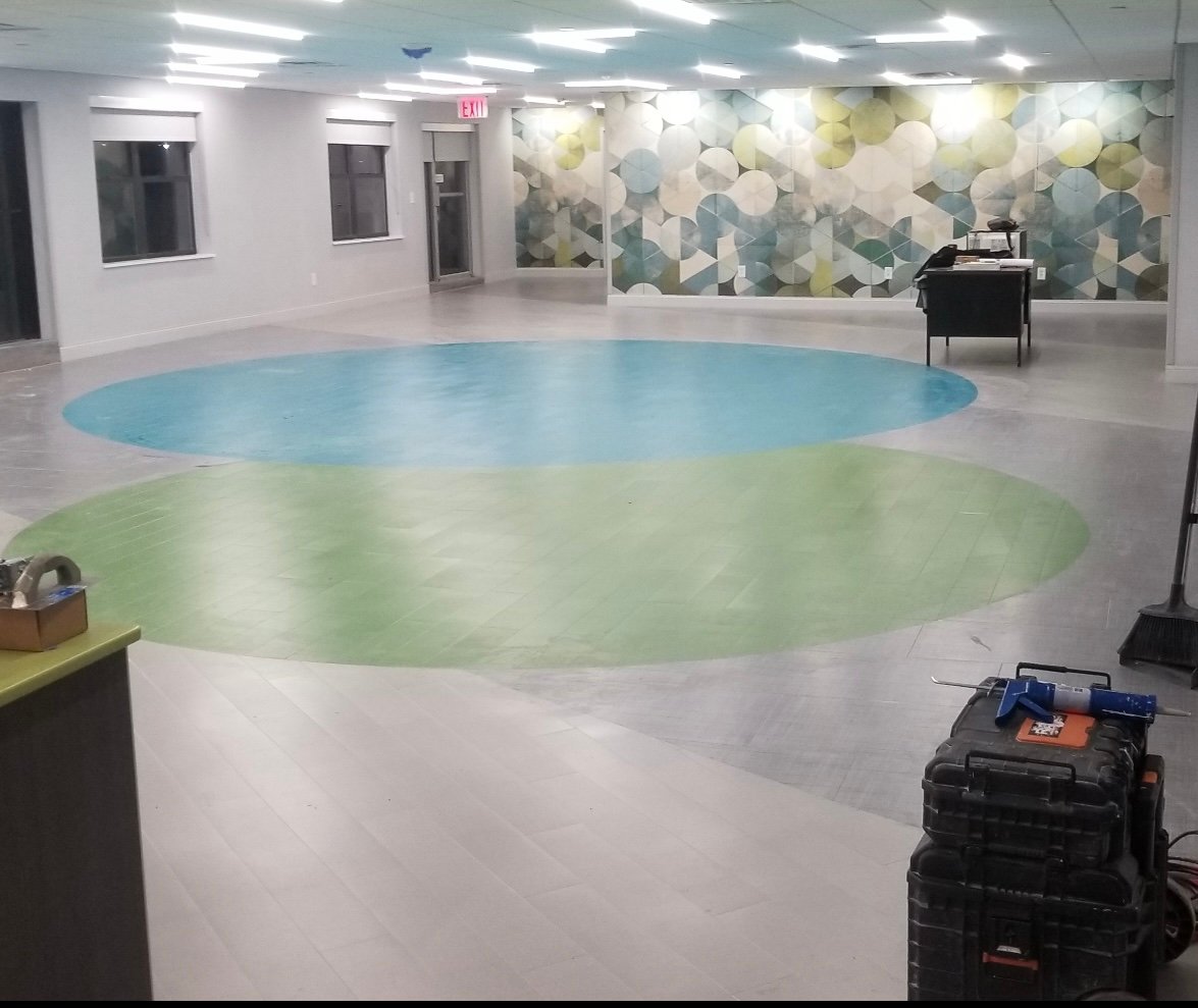 Spacious room with light gray floors, two large blue and green oval carpet areas, and patterned wall art.