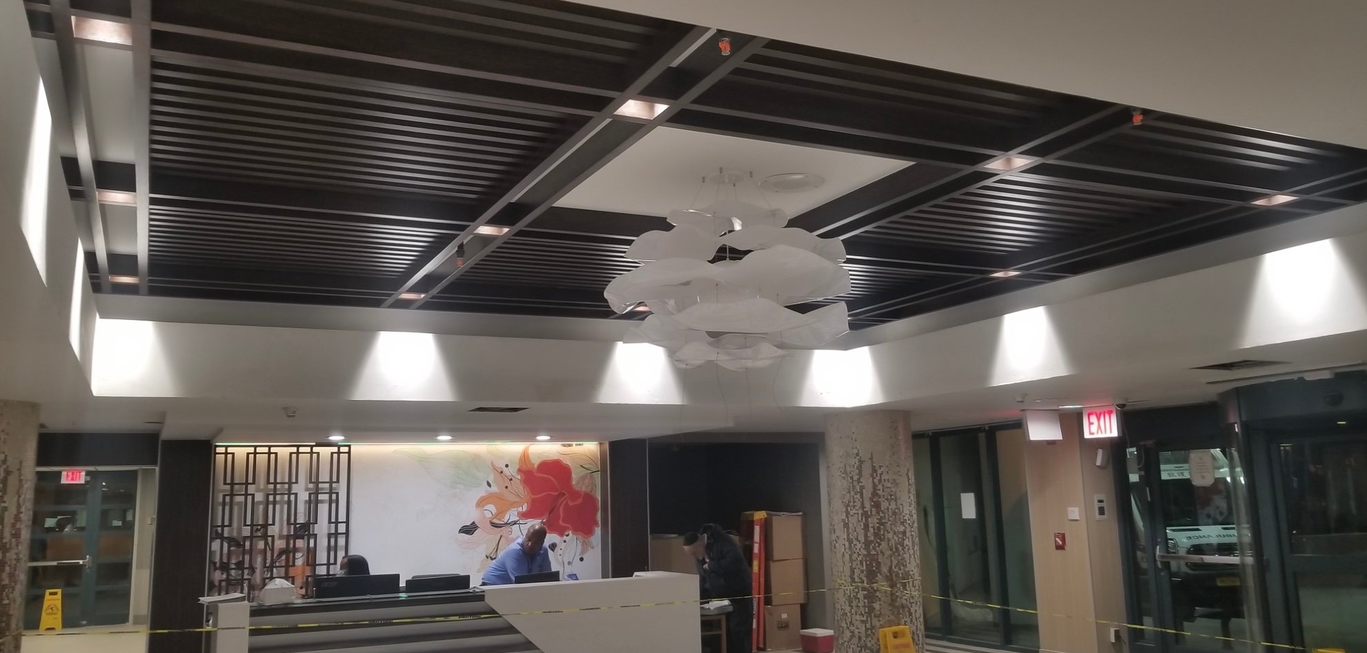 Reception area with black ceiling panels, white chandelier, and two people behind a desk.