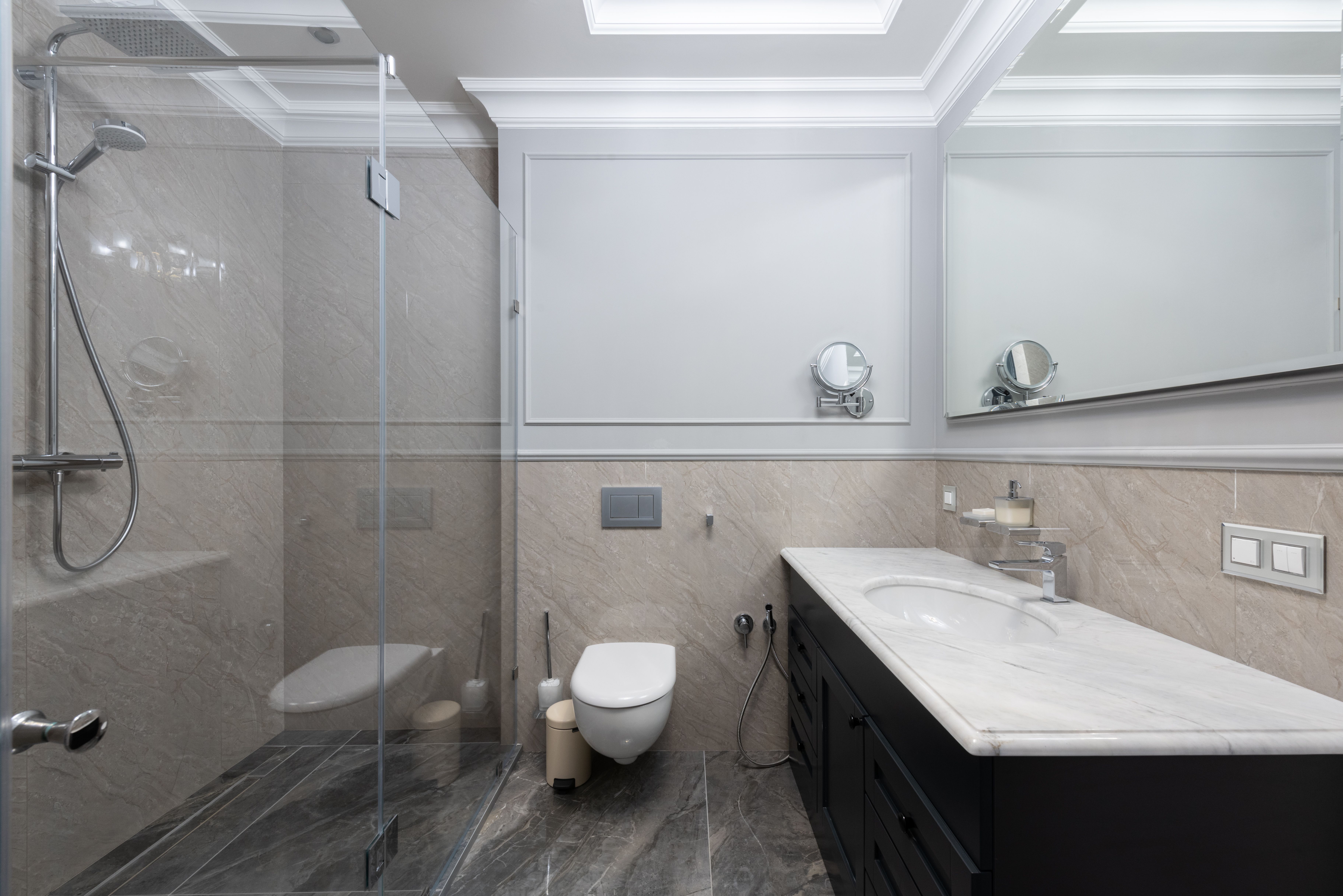 Modern bathroom with glass shower, wall-mounted toilet, and marble sink countertop with black cabinetry.