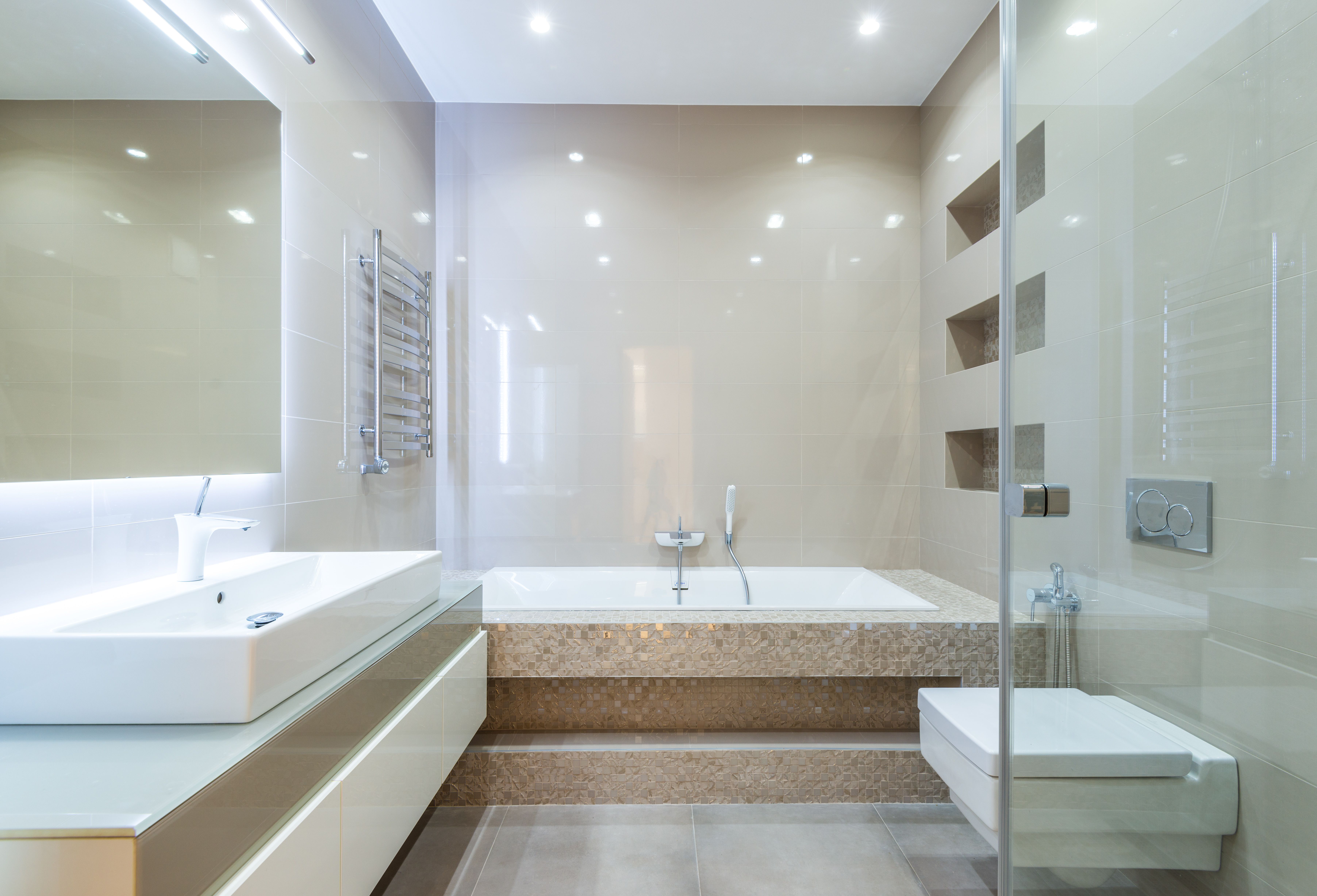 Modern bathroom with white sink, built-in bathtub, and wall-mounted toilet in beige tones.