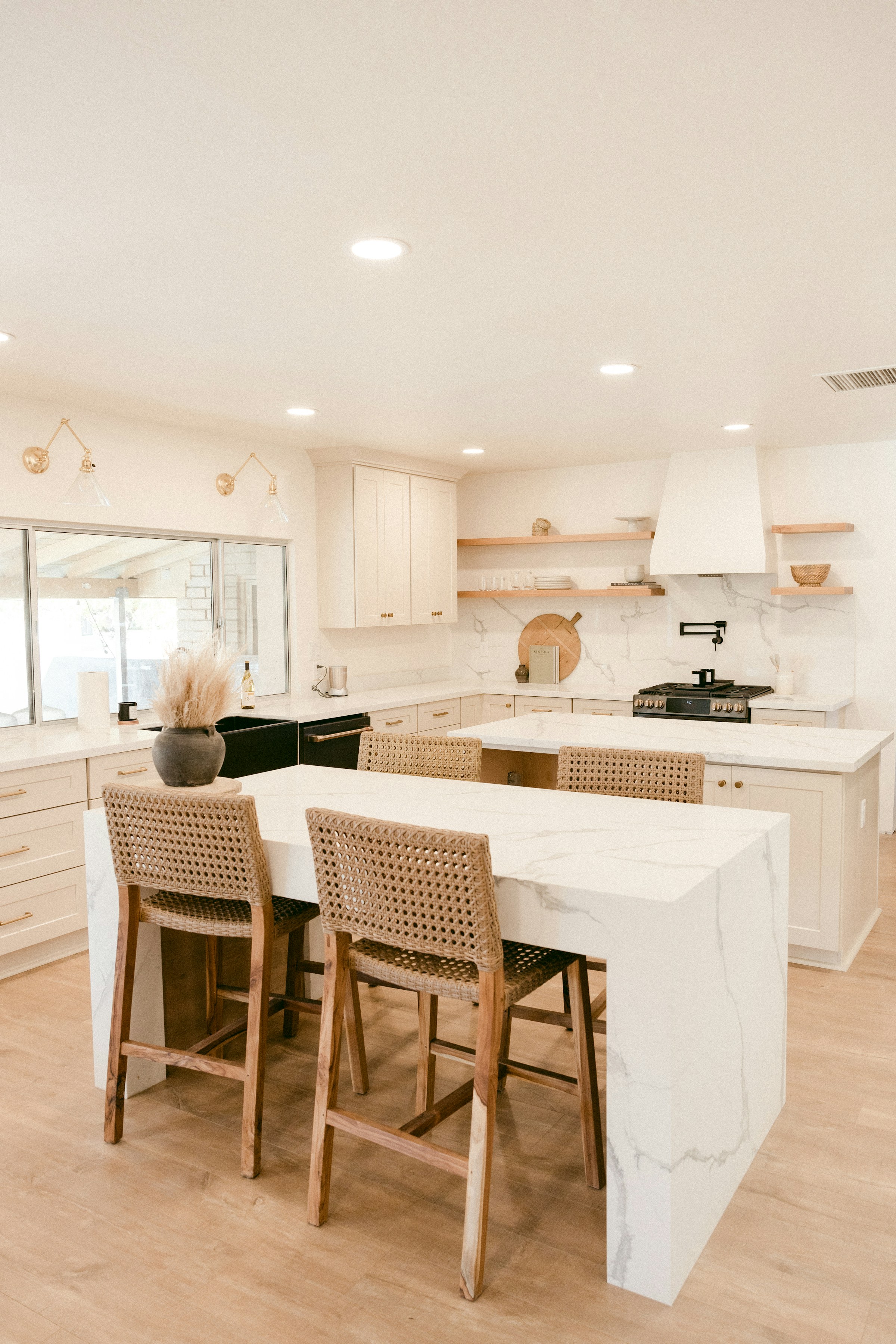 Bright modern kitchen with white marble island and wooden stools featuring woven seats.