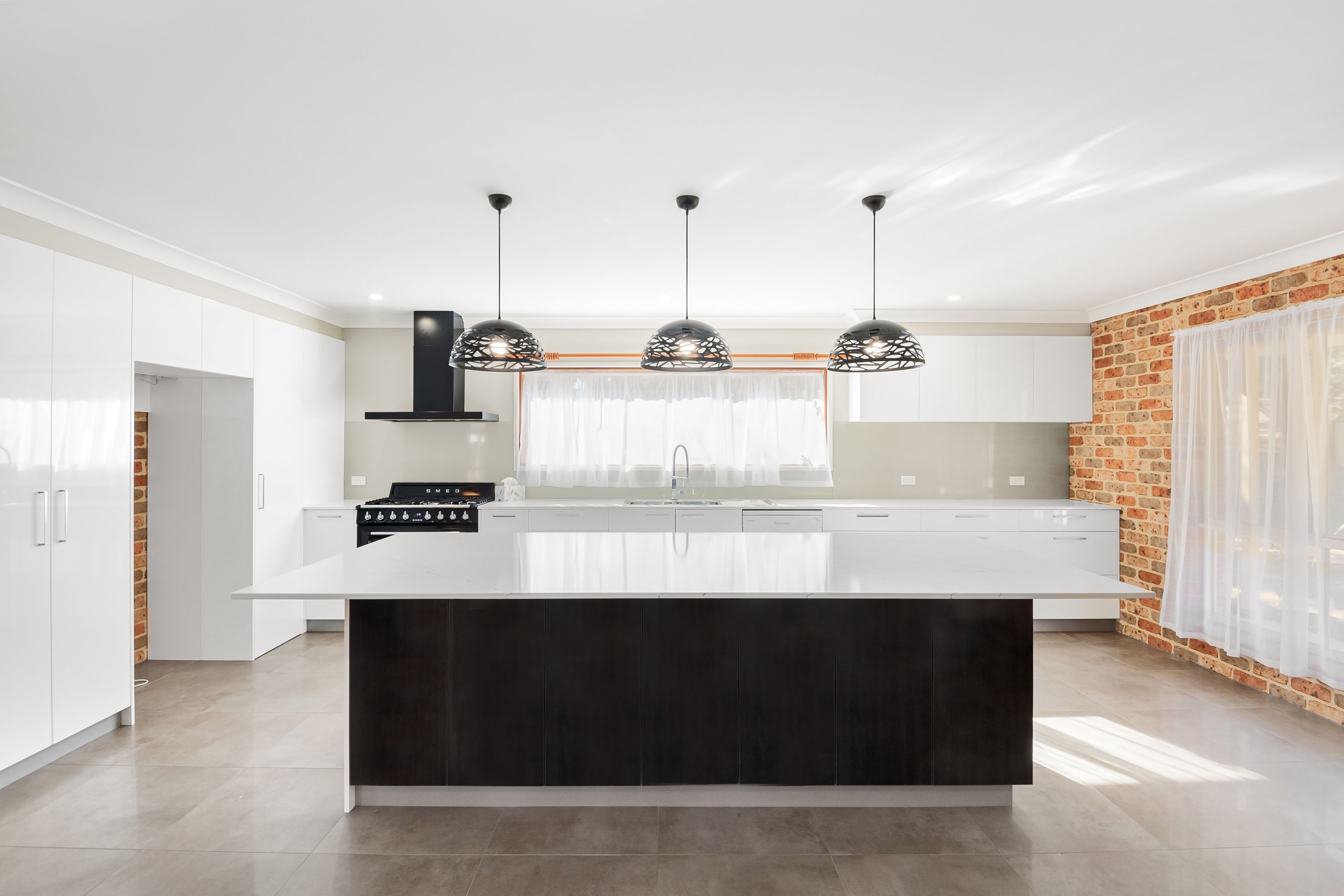 Modern kitchen with white cabinets, large island with dark base, three pendant lights, and brick accent wall.