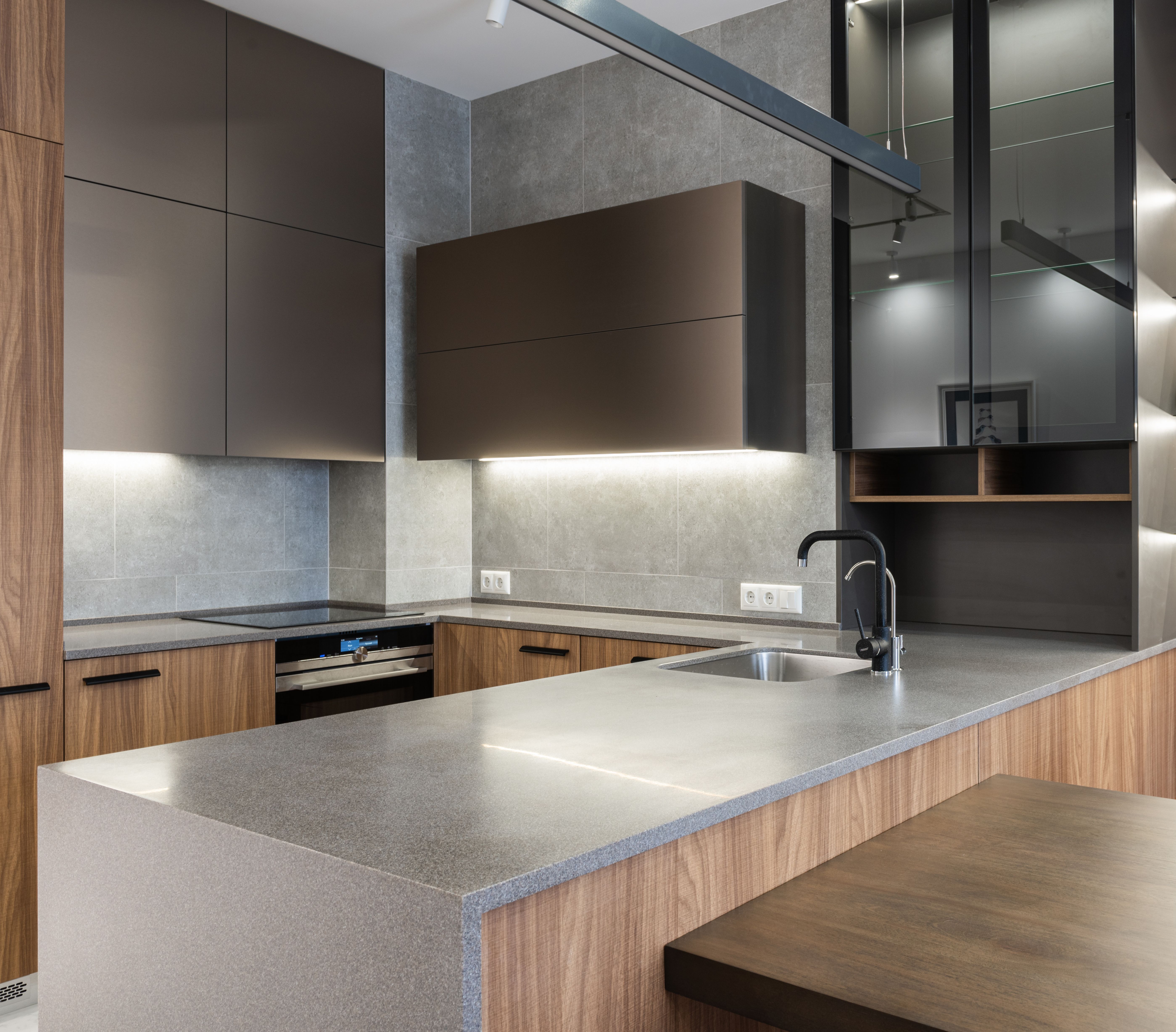 Modern kitchen with wood cabinets, gray stone countertops, built-in oven, and a black faucet on the island.
