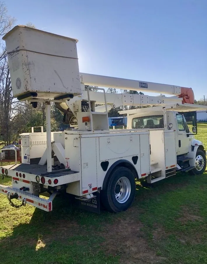 White utility bucket truck with extended boom parked on grassy ground under a clear blue sky.