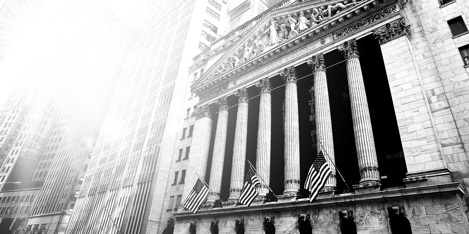 The front facade of the New York Stock Exchange building with six large columns and four American flags.