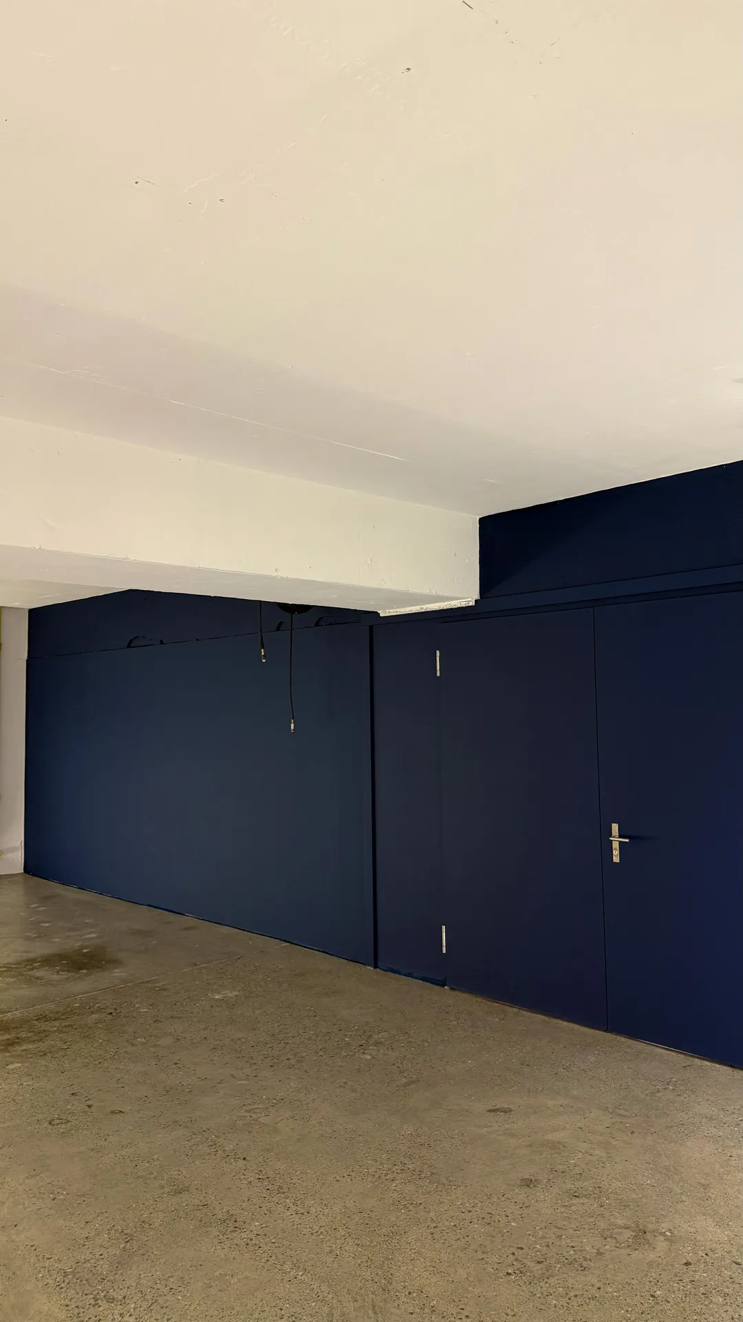 Leerer Raum mit dunkelblauen Wänden und Tür sowie Betonboden und weißer Decke.