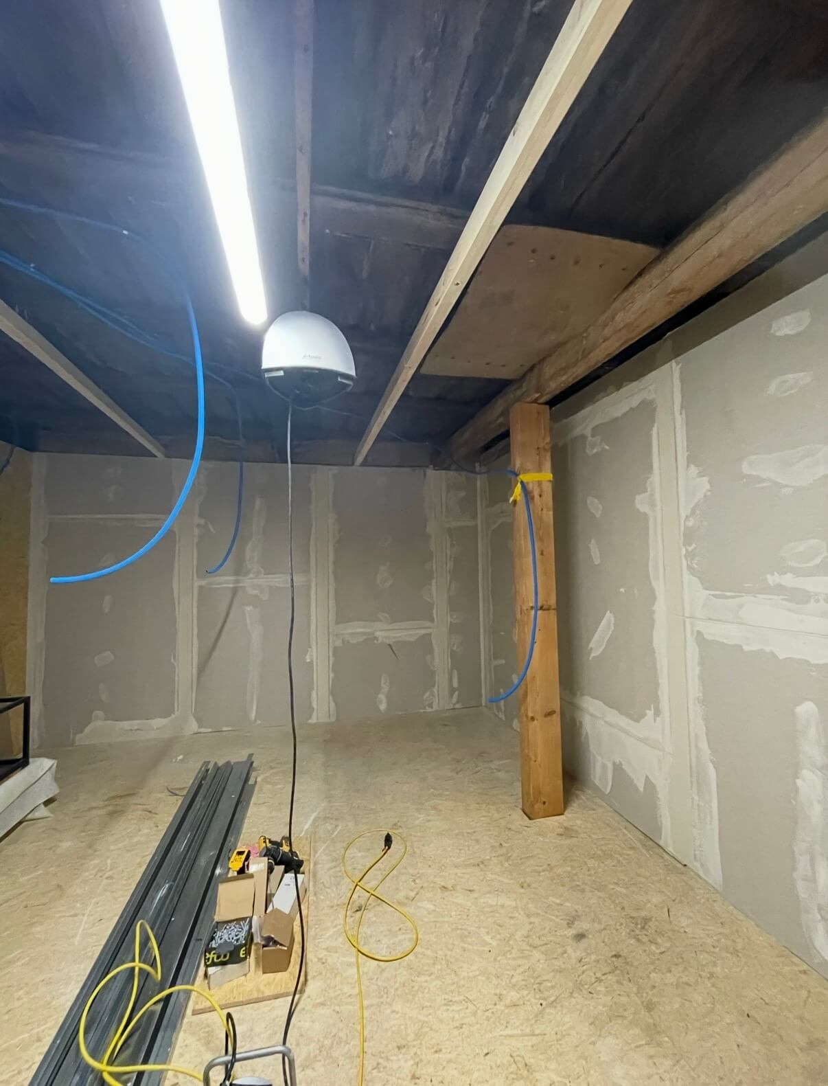 Unfertiger Innenraum mit Holzpfosten, Trockenbauwänden, Bauelementen auf dem Boden und einer Deckenleuchte.