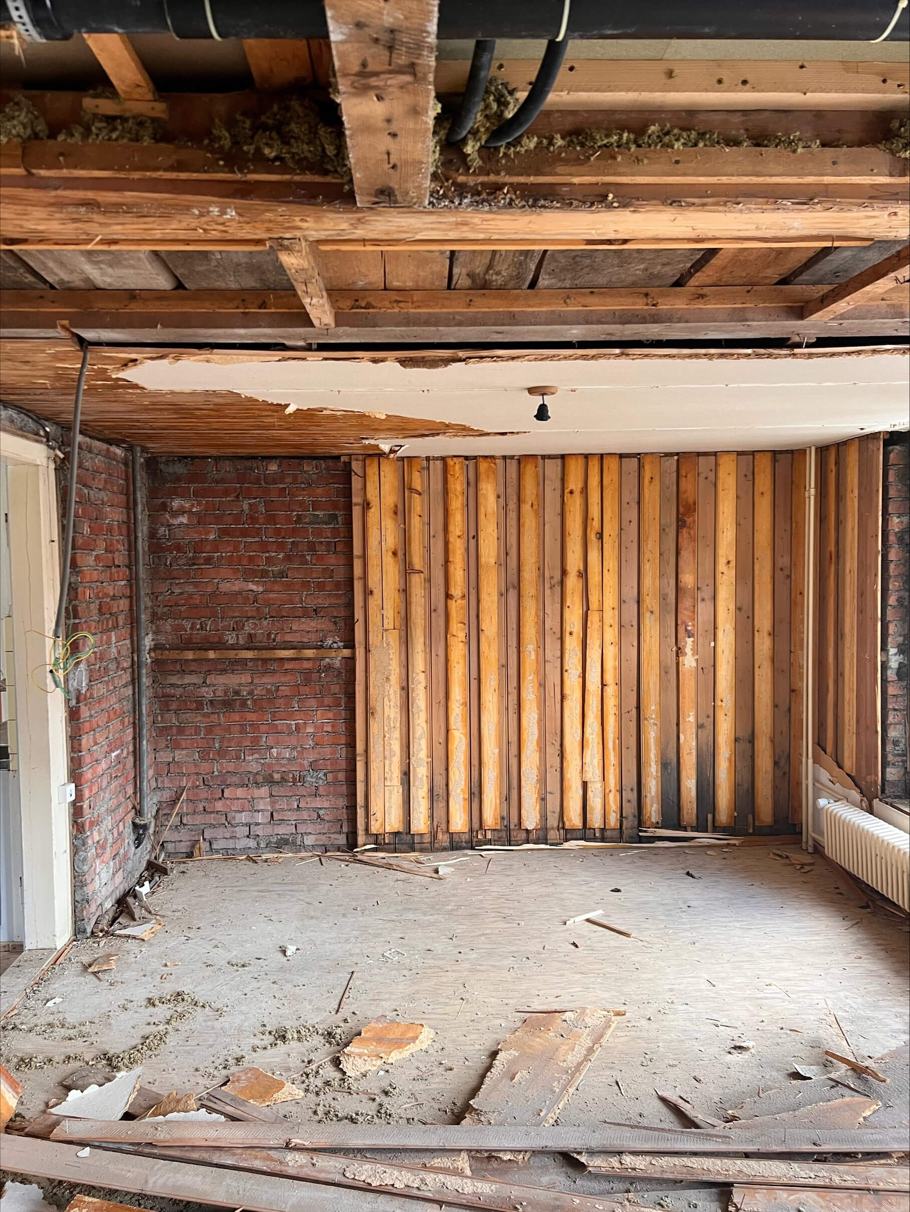 Unrenovierter Dachbodenraum mit freiliegender Dämmung an der Decke und Malerutensilien auf dem Boden vor einem großen Fenster.