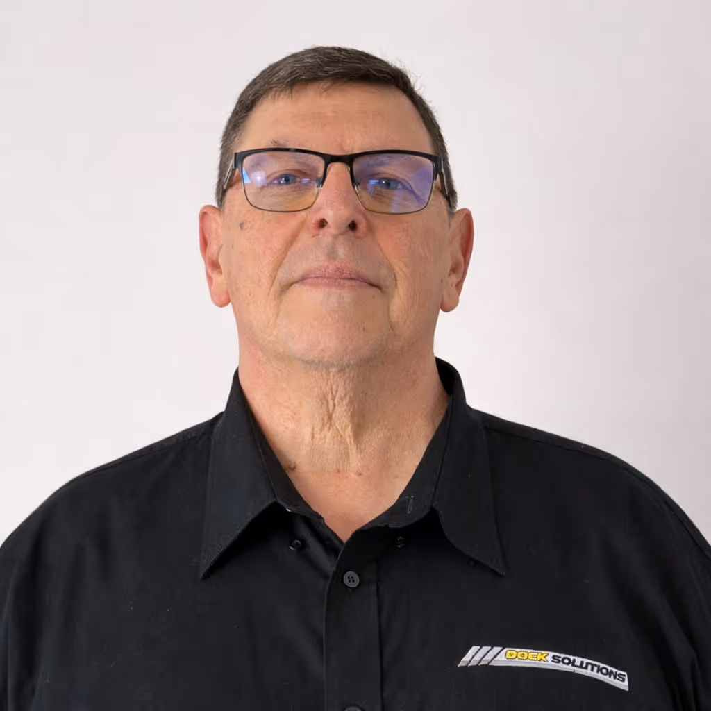 Portrait of a middle-aged man with short dark hair and glasses wearing a black collared shirt with a Dock Solutions logo on the chest, against a plain light background.