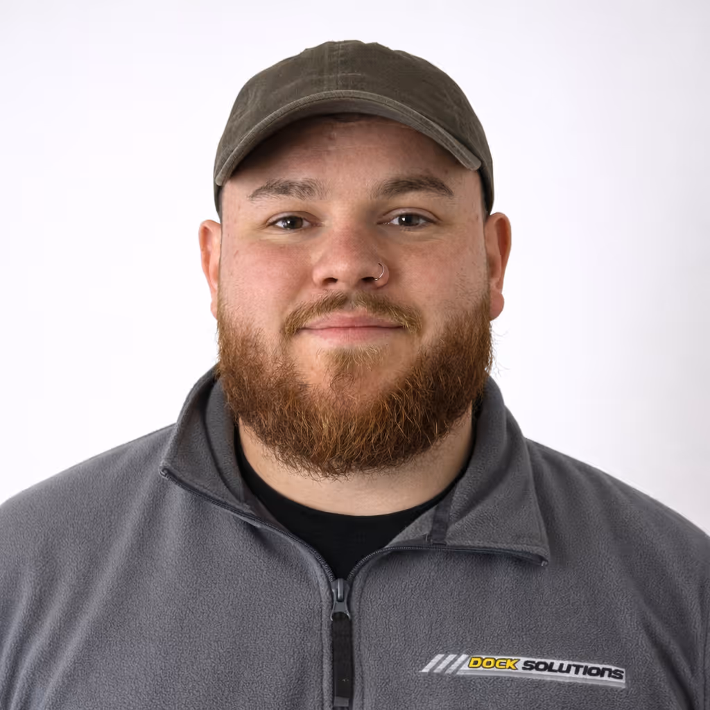 Man with a red beard and wearing a brown cap and gray zip-up jacket with 'Dock Solutions' logo on the chest, against a white background.
