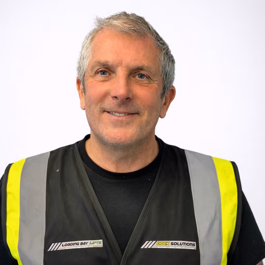 Smiling middle-aged man with short gray hair wearing a black shirt and a high-visibility safety vest with Loading Bay Lifts and Dock Solutions logos on the chest.