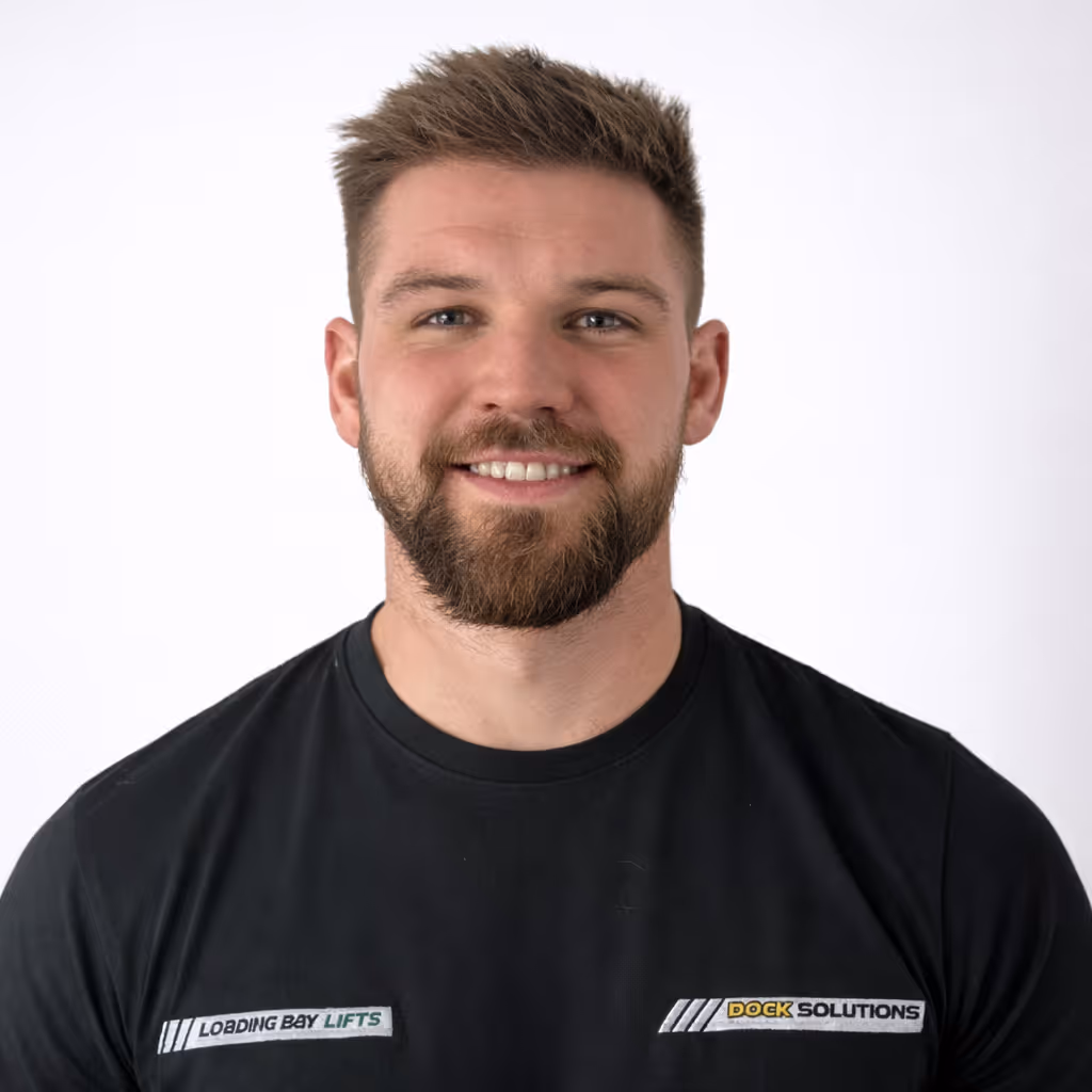 Smiling man with short brown hair and beard wearing a black shirt with logos reading 'Loading Bay Lifts' and 'Dock Solutions' on a white background.
