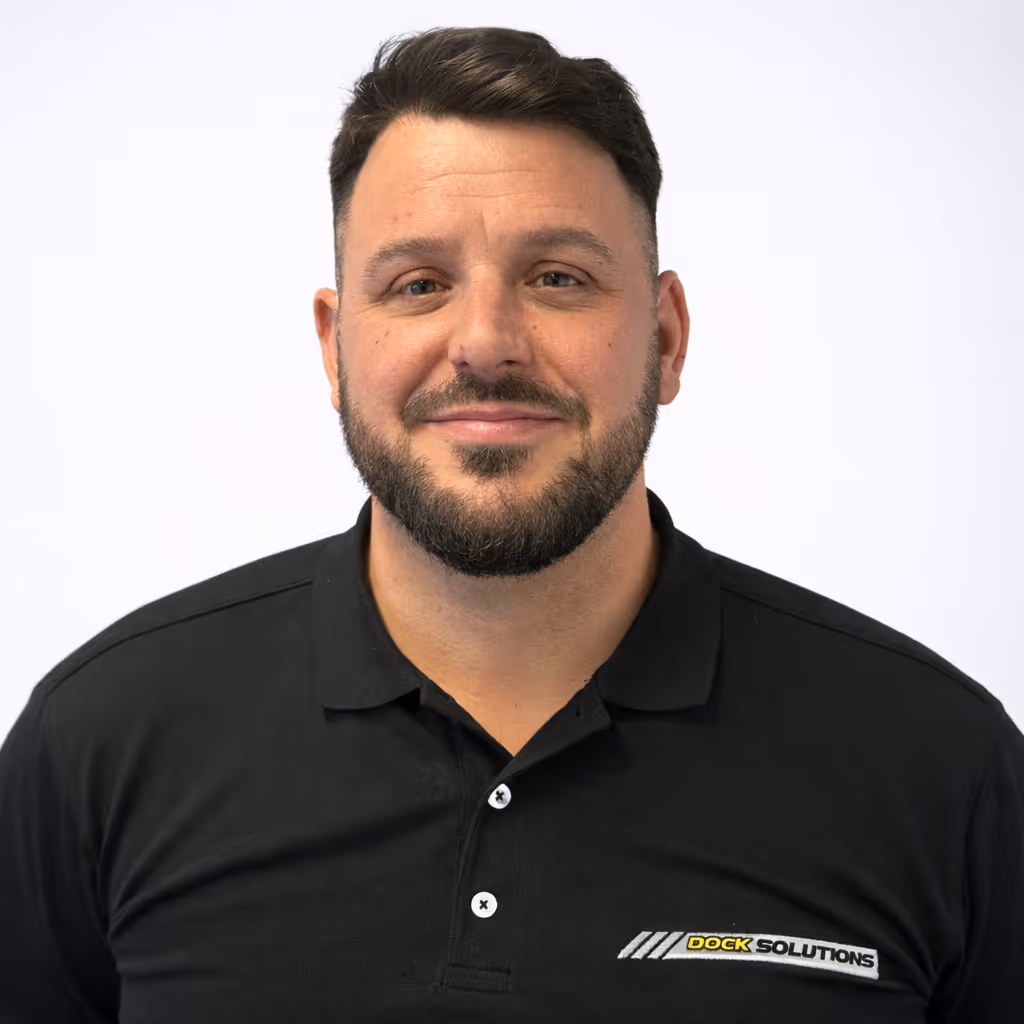 Man with short dark hair and beard wearing a black polo shirt with 'Dock Solutions' logo on the chest, smiling against a plain white background.