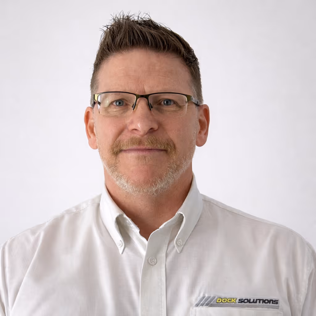 Man with short brown hair, glasses, and light facial hair wearing a white button-up shirt with 'Dock Solutions' logo on the chest, against a plain light background.