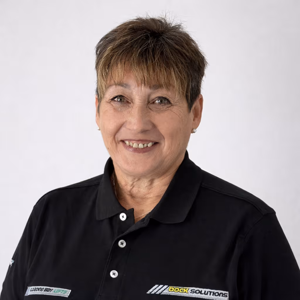 A smiling middle-aged woman with short brown hair wearing a black polo shirt with a Dock Solutions logo on it, posing against a plain light background.