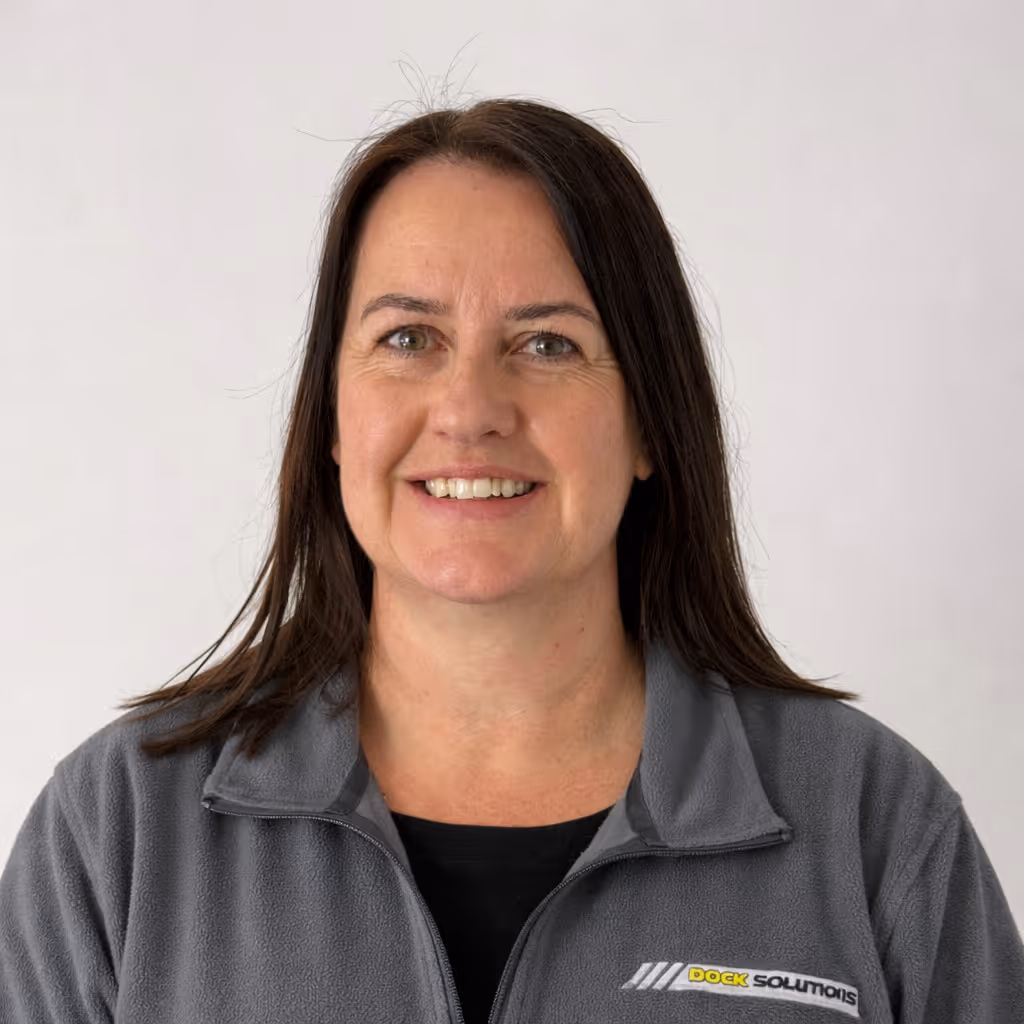 Smiling woman with long dark hair wearing a gray fleece jacket with a Dock Solutions logo on the chest against a plain light background.