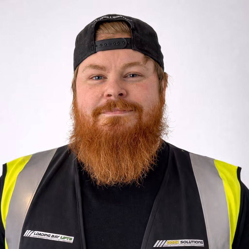 Man with a red beard wearing a black backward cap and a black and yellow high-visibility vest with Loading Bay and Dock Solutions logos.