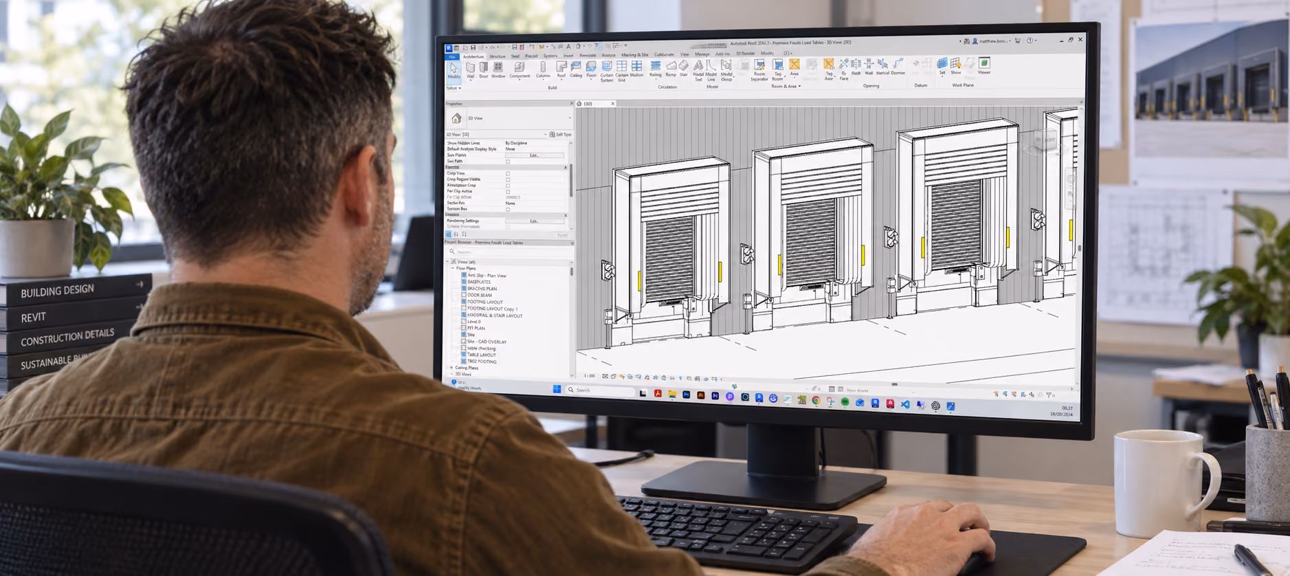 Person working on a desktop computer with a large monitor displaying architectural 3D modeling software showing detailed building door designs, in a bright office with plants and design boards in the background.