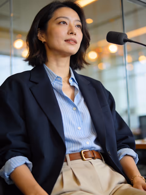Confident woman in business attire speaking into a microphone in an office setting.