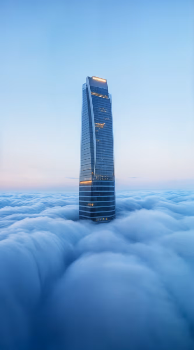 Modern skyscraper rising above thick clouds under a clear blue sky.