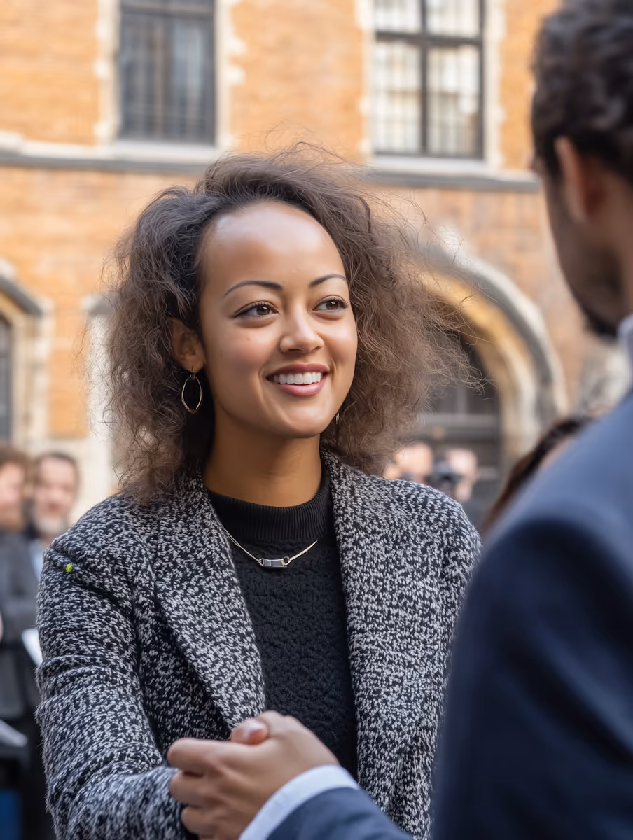 Smiling woman with curly hair shaking hands with a man outdoors in an urban setting.