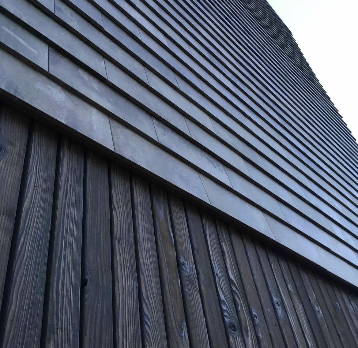 Close-up of a building's exterior featuring dark vertical wooden panels below and overlapping horizontal metal panels above.
