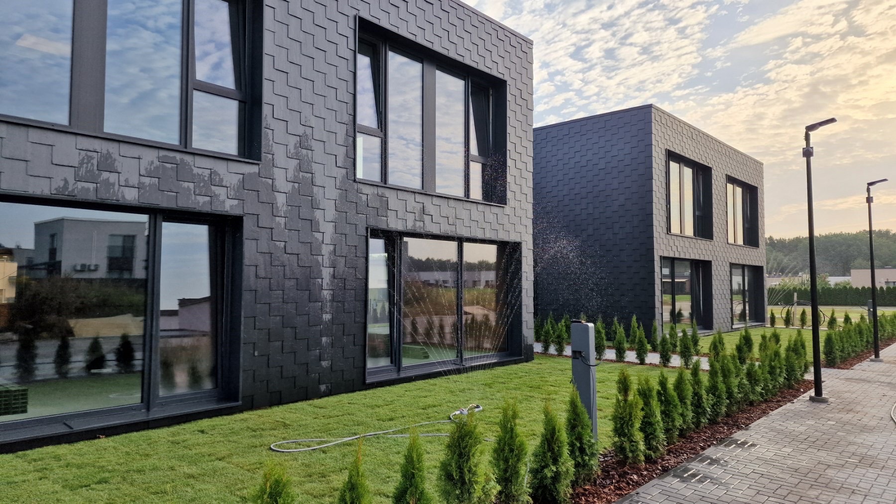 Modern black building with large reflective windows, green lawn, and sprinkler watering plants.
