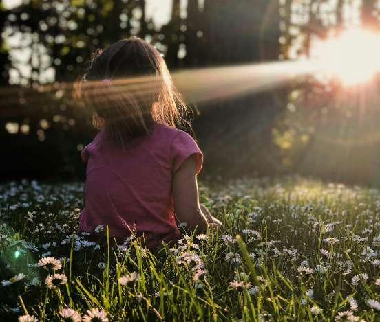 Kind sitzt bei Sonnenuntergang in grüner Natur