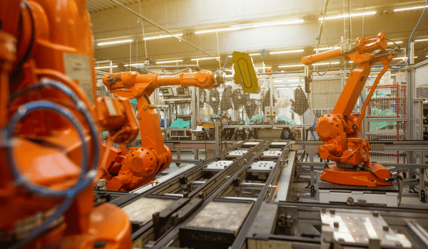 Orange industrial robotic arms working on a production line in a factory with metal components.