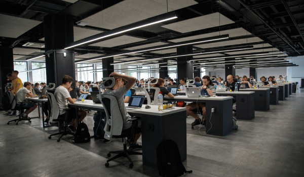 Large open office space with rows of people working on laptops at desks under modern lighting.