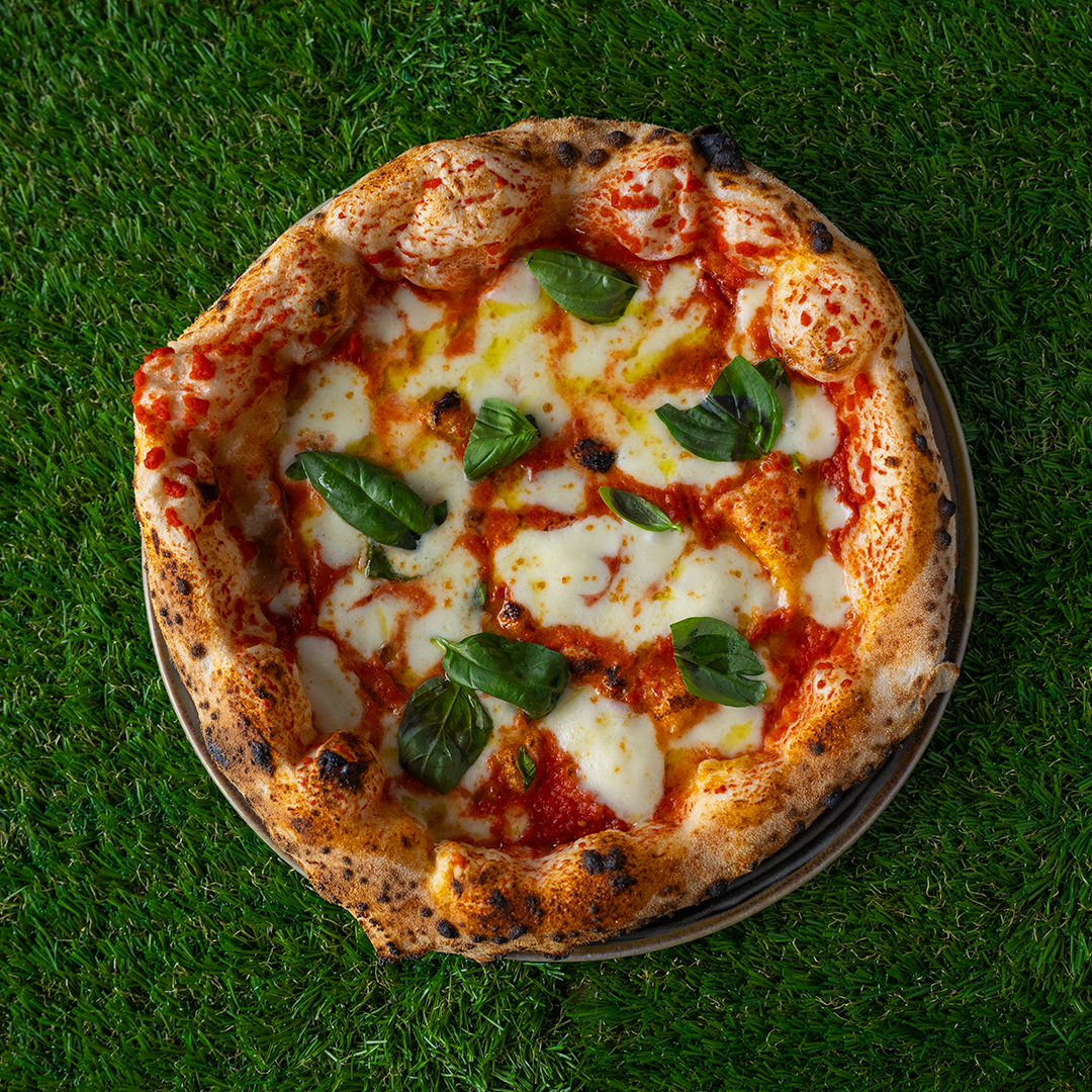 Pizza Margherita con mozzarella fusa, salsa di pomodoro e foglie di basilico fresca su una crosta croccante, posta su un piatto su prato verde.