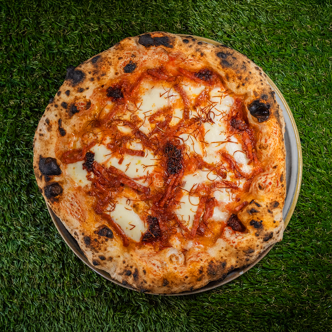 Pizza Diavola con mozzarella, salsa di pomodoro e fette di salame piccante su uno sfondo di erba verde.