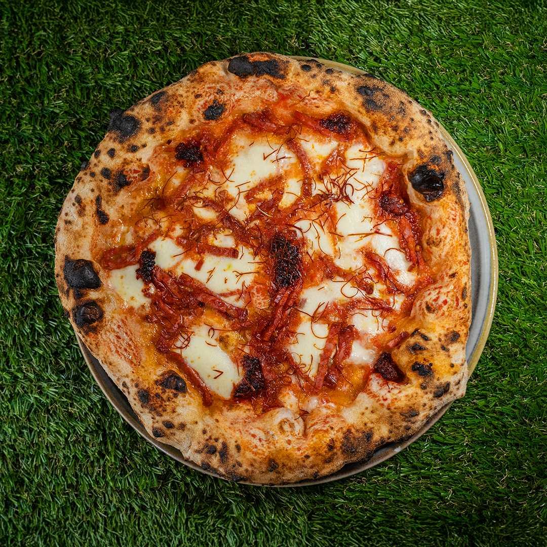 Pizza Diavola con mozzarella, salsa di pomodoro e fette di salame piccante su uno sfondo di erba verde.