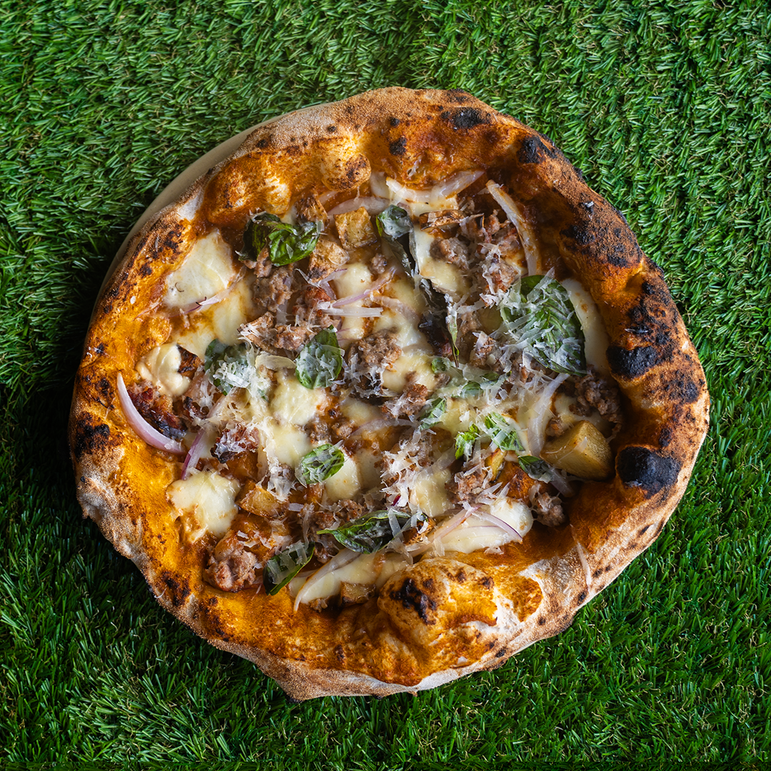 Pizza con formaggio fuso, carne macinata, foglie di basilico e cipolla su sfondo di erba verde.