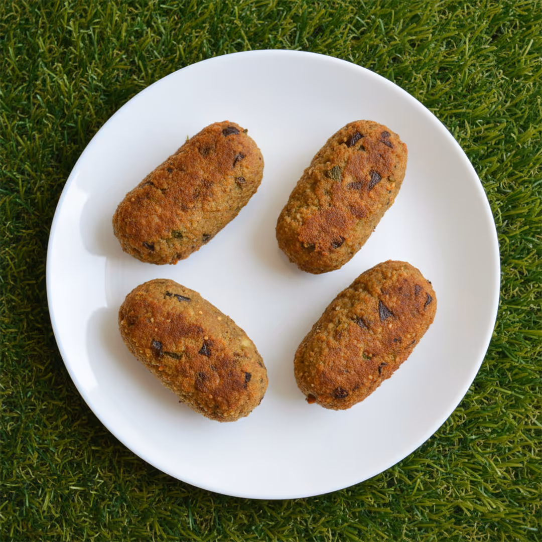 Quattro crocchette dorate con pezzi di melanzane su un piatto bianco, posato su erba verde.